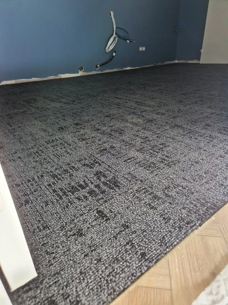 Pose de dalles moquettes. Les fibres de la moquette procurent un excellent niveau d'isolation phonique. Elle contribue ainsi à réduire le bruit, notamment l'impact des pas. 